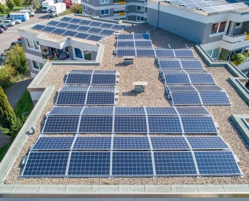 A rooftop with 56 solar panels and a roof in the background with more solar panels with a parking lot to the left