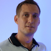 Headshot of a man wearing a white shirt with a dark blue collar and looking at the camera with a neon blue light background